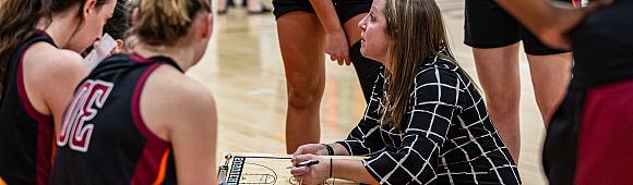 Image of women's basketball coach talking to players on the bench.